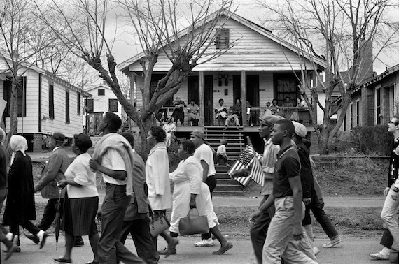 Selma marchers passing by house with people, negro and white. Man holding small American flag. Selma to Montgomery, Alabama civil rights march. March 25, 1965